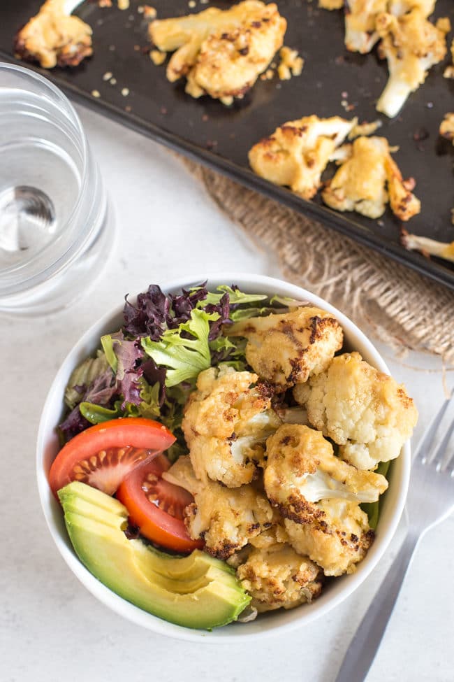 Hummus roasted cauliflower in a bowl with lettuce, tomato and avocado, shot from above