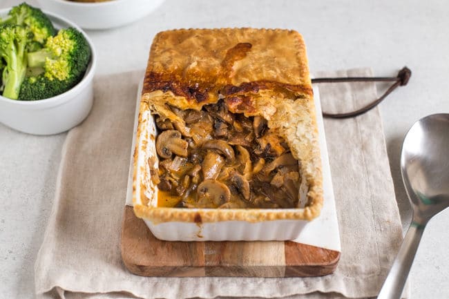 Mushroom stroganoff pie, served on a wooden board, with a scoop removed