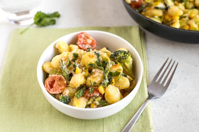 Landscape photo of colourful gnocchi primavera with broccoli, asparagus and tomatoes, on a green linen