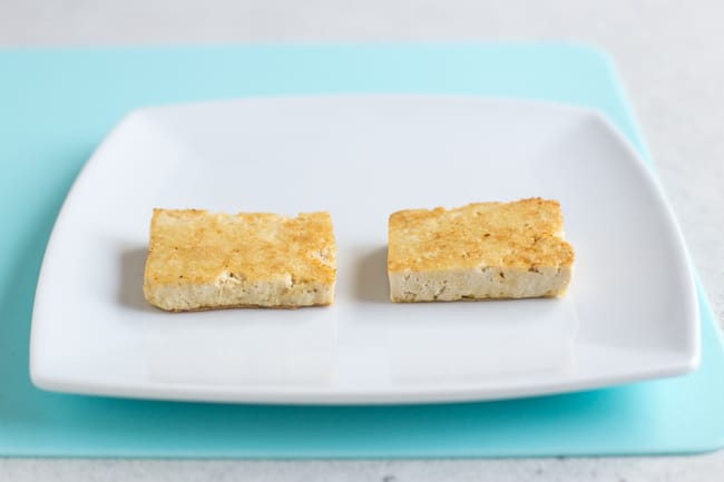Two pieces of golden tofu on a white plate on a pale blue board