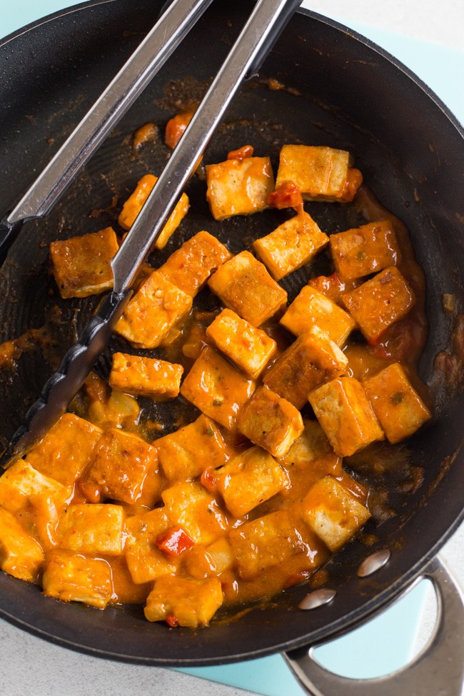 Crispy tofu cubes in a frying pan with a red Thai sauce