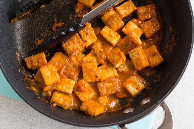 Diced tofu in a frying pan, coated in an red Thai sauce