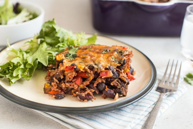 A portion of cheesy vegetarian chilli and rice bake on a plate with salad