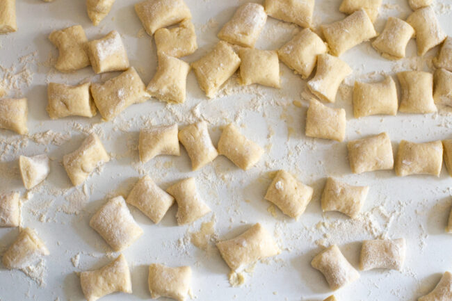 Uncooked ricotta gnocchi scattered across a white surface.