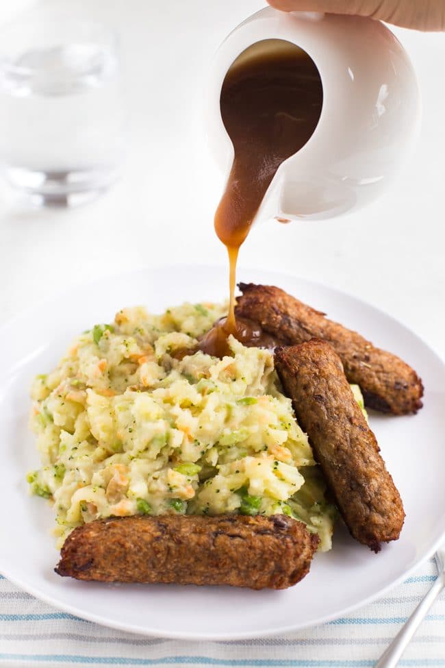 Mashed potato and vegetarian sausages with gravy being poured