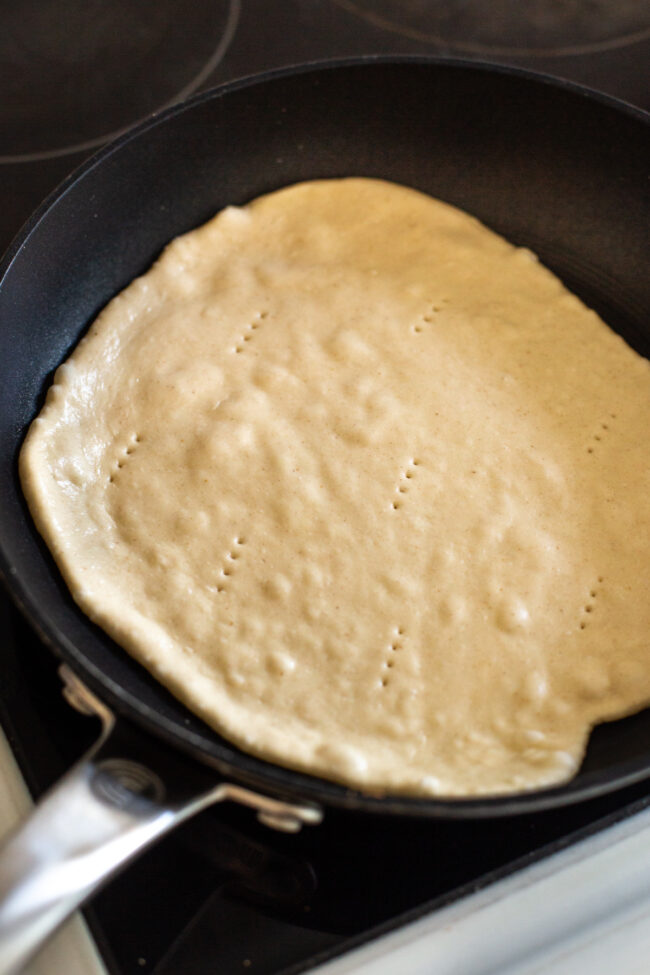 Raw flatbread cooking in a frying pan, pricked with a fork.