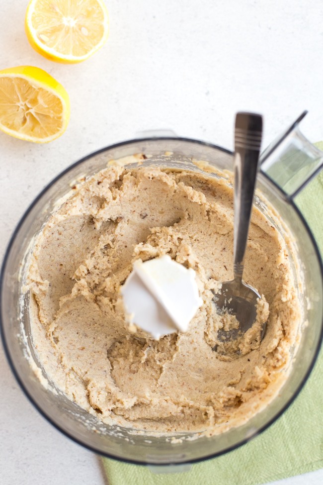 Low-carb cauliflower hummus in a food processor with lemon wedges