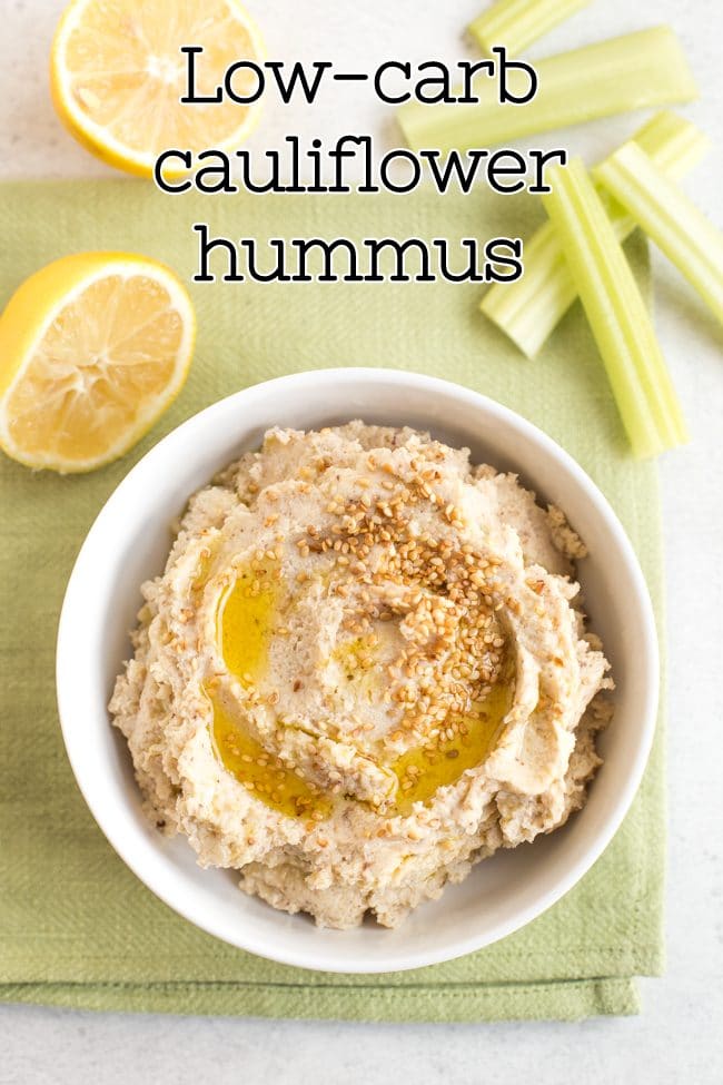 Low-carb cauliflower hummus topped with toasted sesame seeds, served with lemon wedges and celery sticks