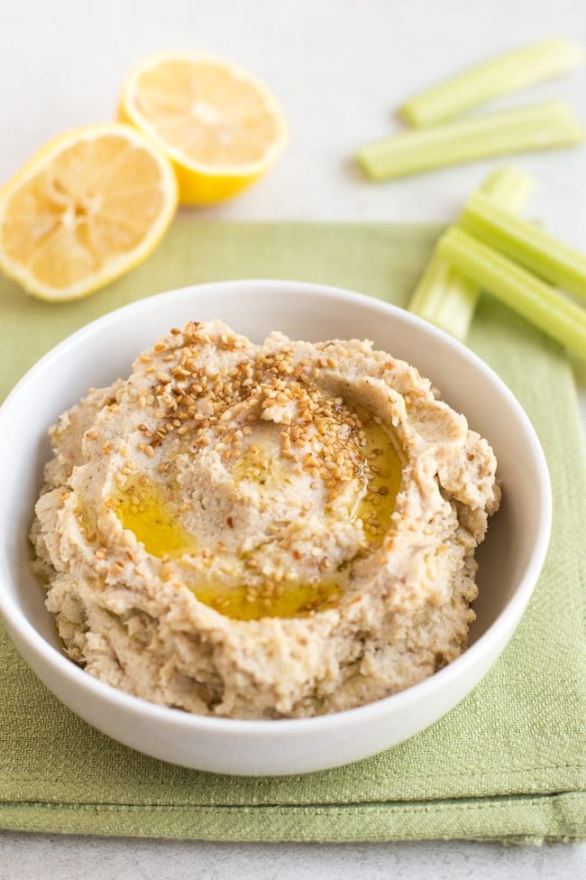 Low-carb cauliflower hummus in a white bowl with lemon wedges and celery sticks