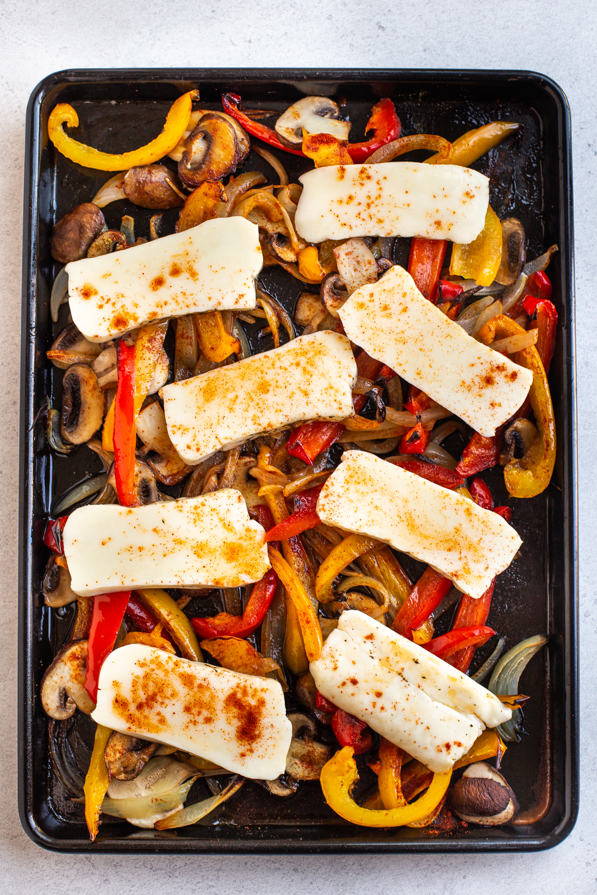 Roasted vegetables on a baking tray, topped with sliced halloumi cheese.