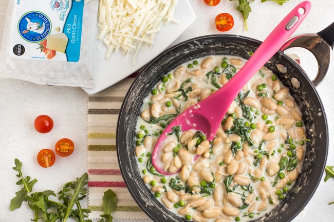 Creamy white beans in a frying pan with goat's cheese and peas