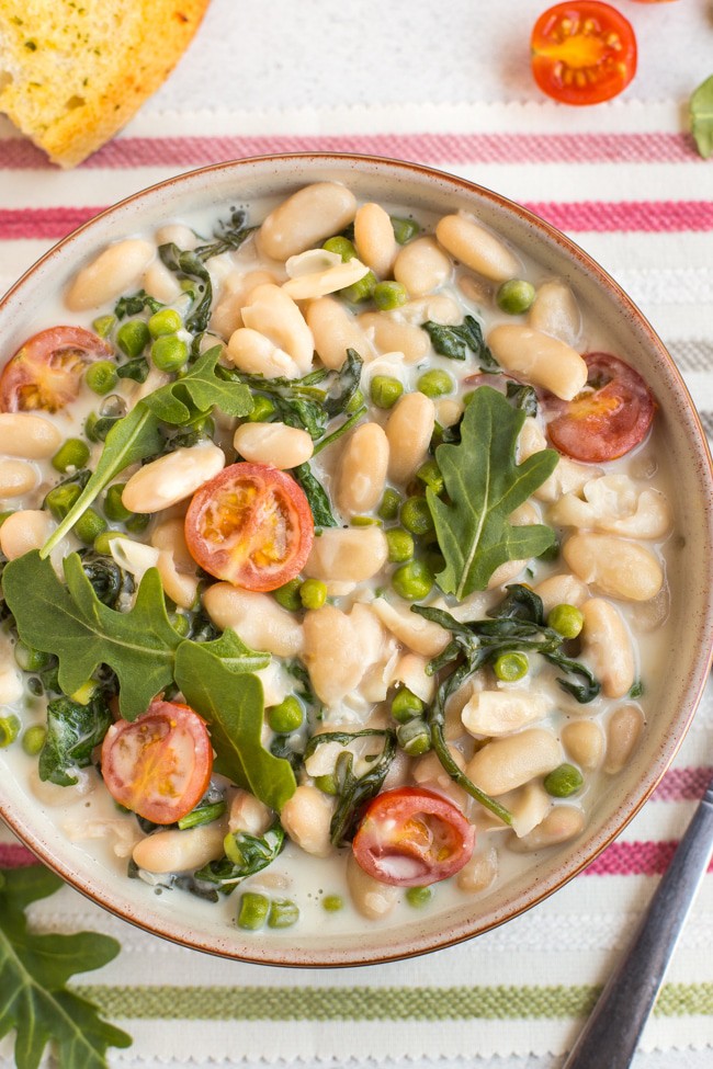 Close up of creamy white beans with tomatoes and rocket in a bowl
