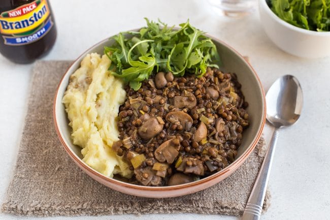 Portion of lentil and mushroom stew in a bowl with cheesy mashed potato and rocket