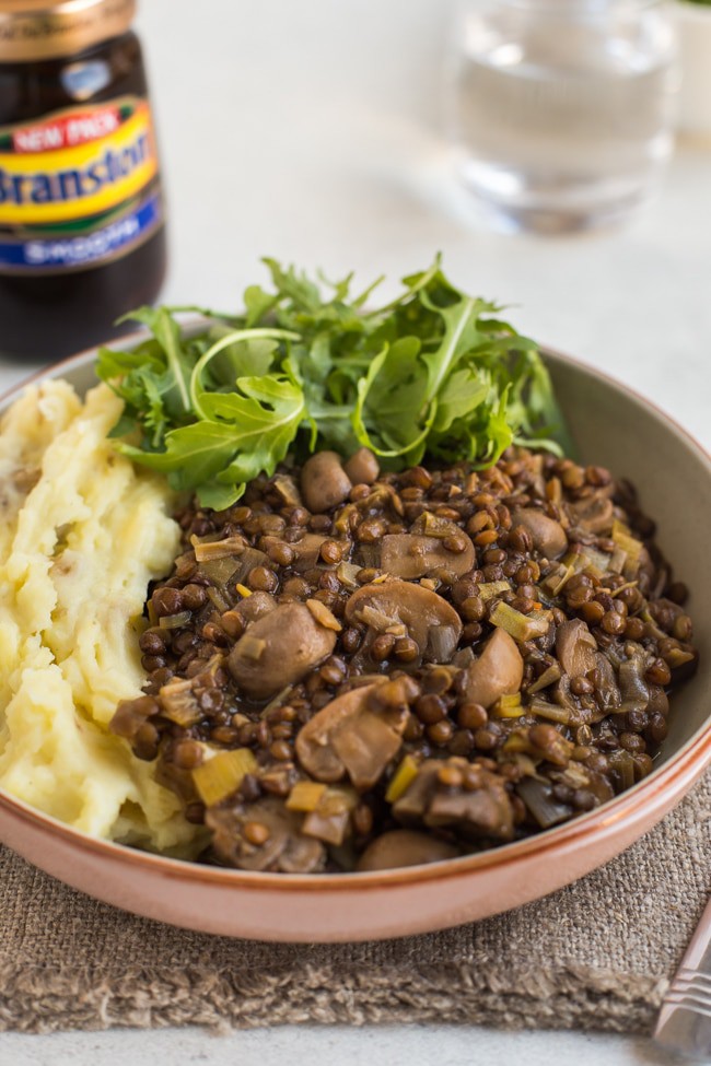 Lentil and mushroom stew in a bowl with cheesy mashed potato and rocket