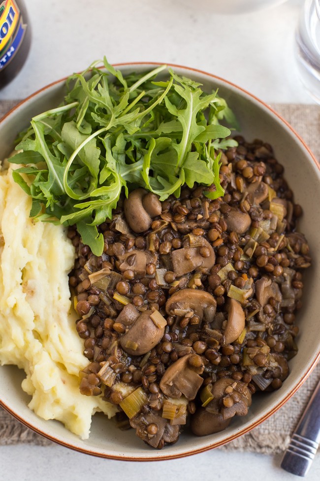 Lentil and mushroom stew in bowl with cheesy mashed potato and rocket