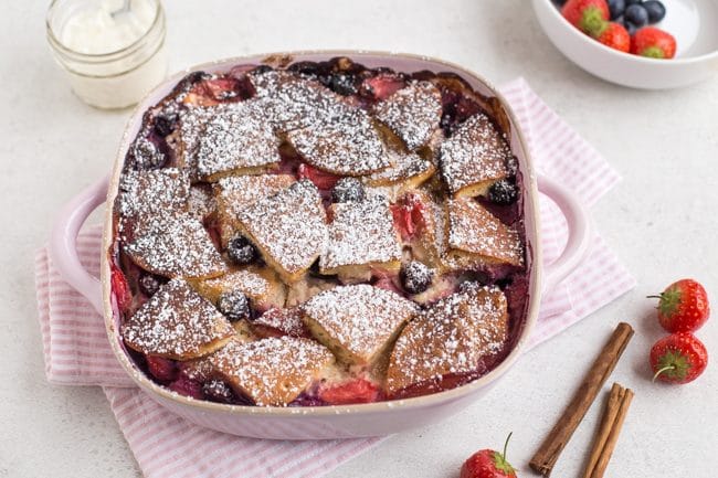 Baked pancake pudding in a baking dish with fresh fruit and cinnamon sticks