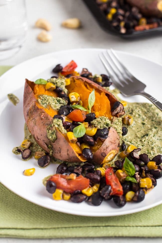 A vegan loaded sweet potato on a plate with roasted black beans and homemade pesto