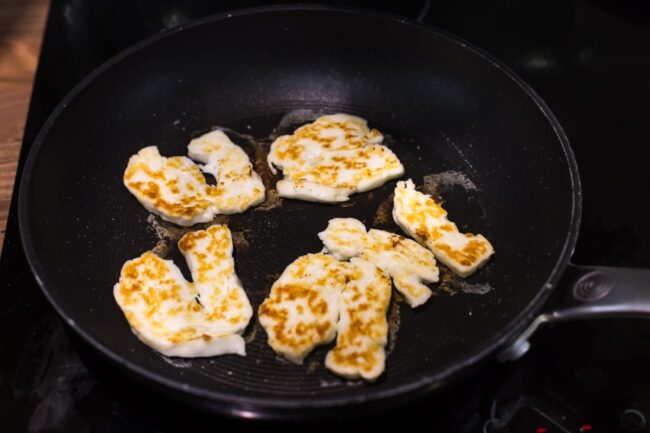 Slices of halloumi cheese cooking in a frying pan