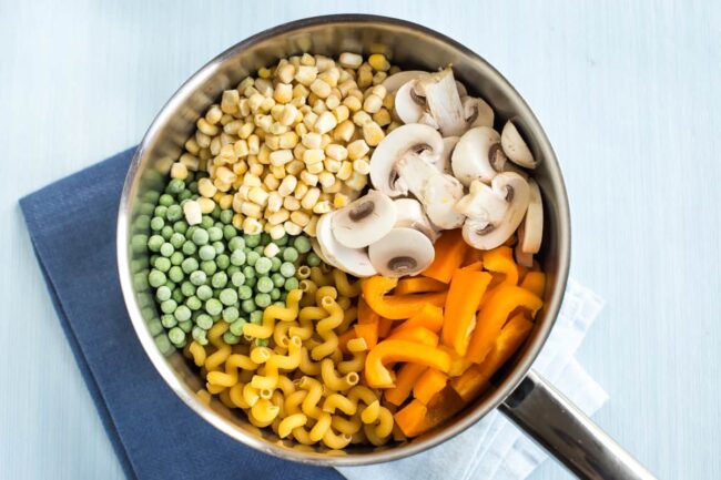 Uncooked pasta and vegetables in a saucepan.