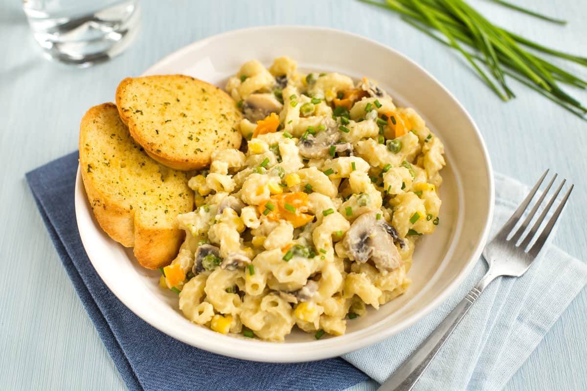 Portion of creamy veggie pasta in a bowl with garlic bread.