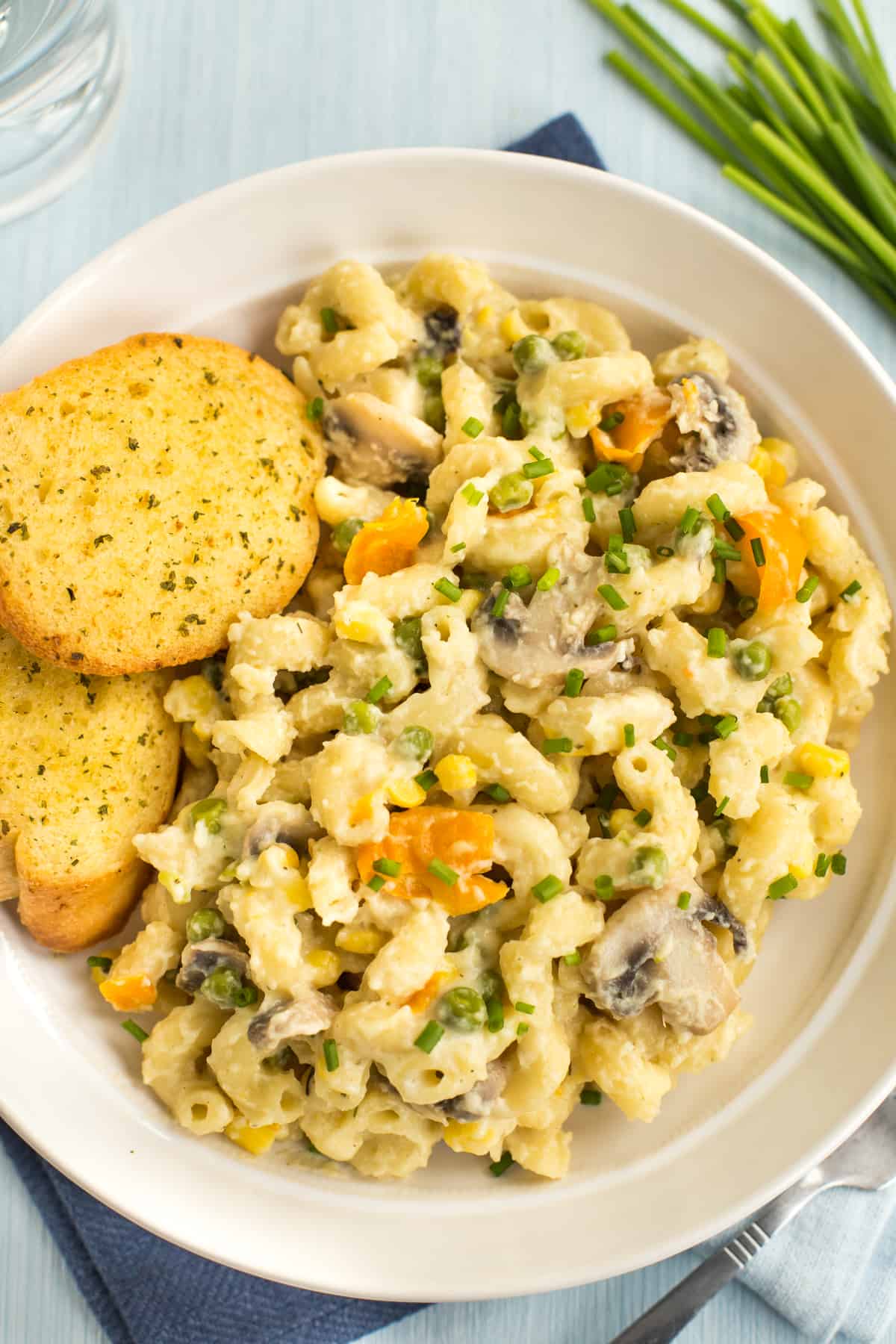 Portion of creamy veggie pasta in a bowl with garlic bread and chives.