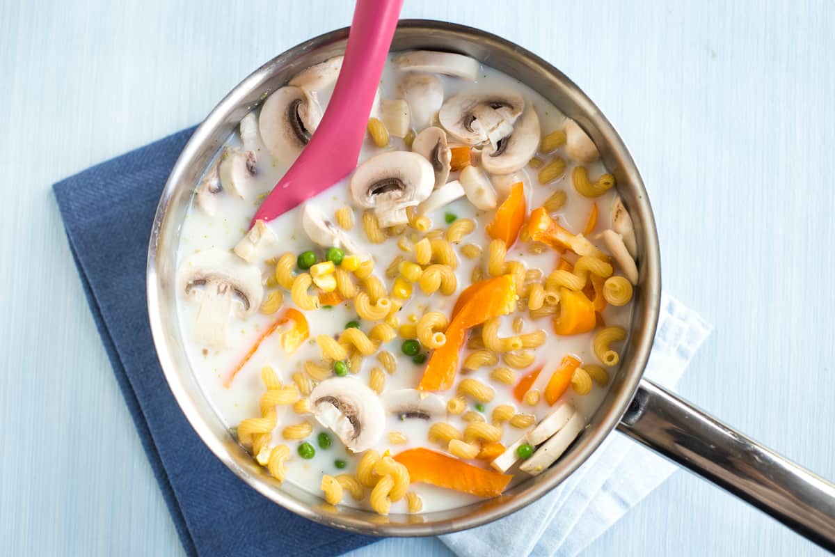 Uncooked pasta and vegetables in a saucepan with milk.