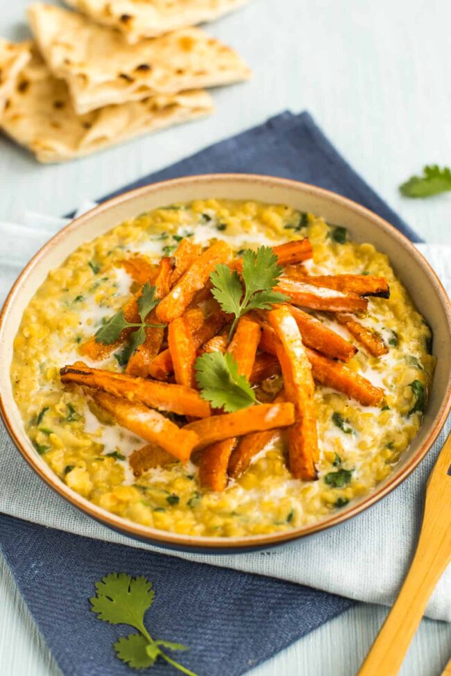 Portion of creamy lentil dal in a bowl topped with roasted carrots, coconut milk and cilantro.