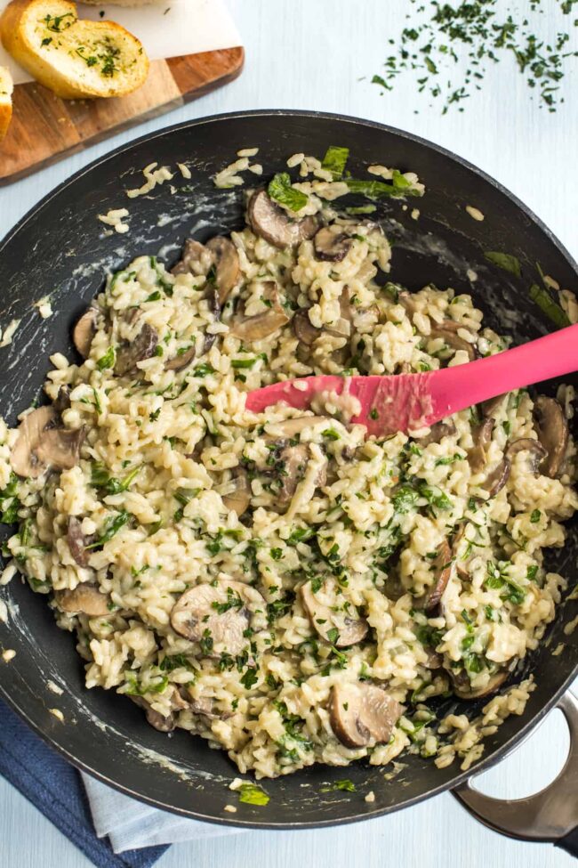 Mushroom risotto in a wok with spinach and parsley.