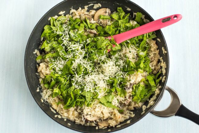 Risotto in a wok topped with fresh spinach and grated cheese.