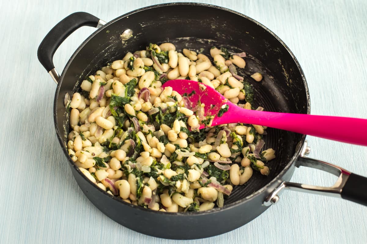 White beans cooking in a pan with spinach.