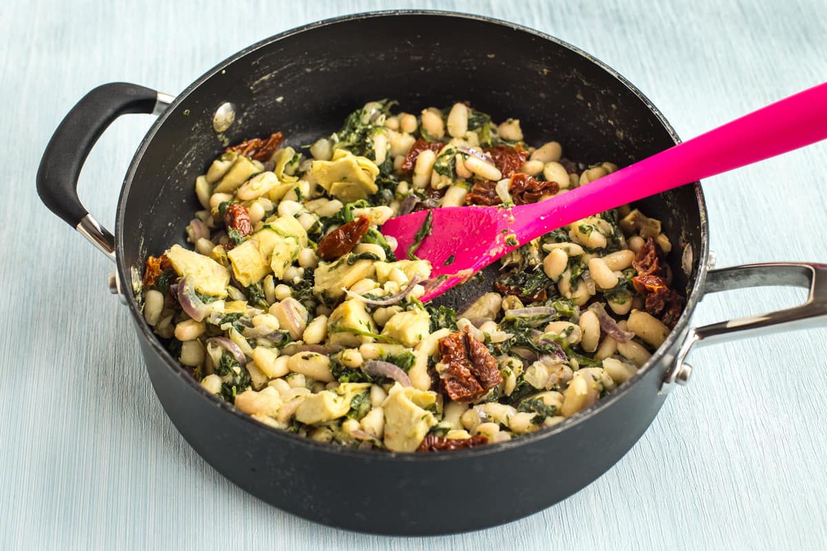 Tuscan white beans in a pan with spinach and sun-dried tomatoes.