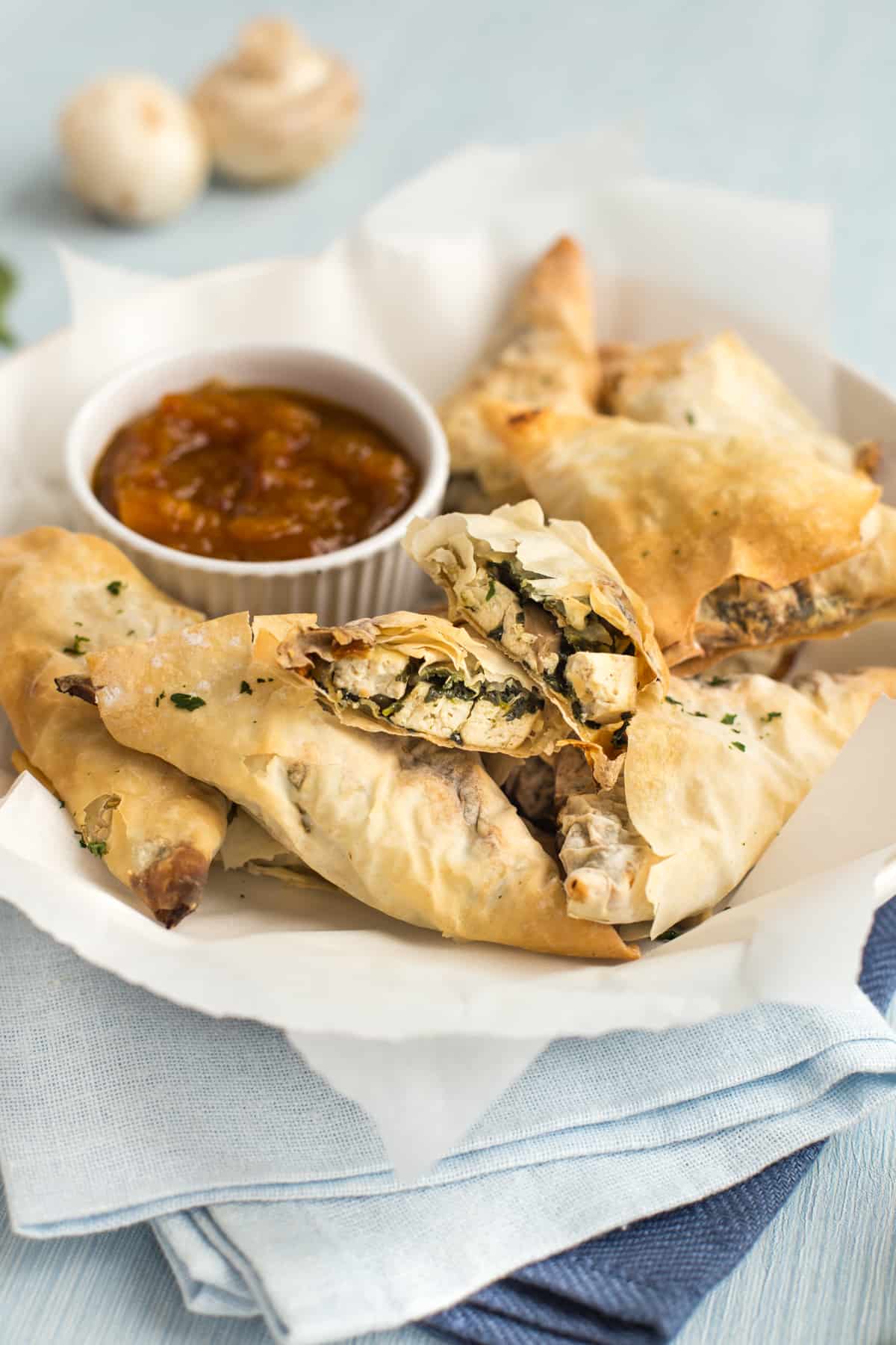 A bowlful of crispy homemade samosas, with one torn open to show the tofu and spinach filling.