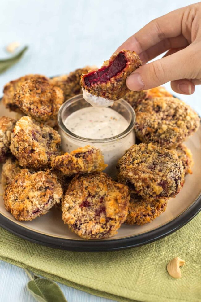 A crispy beetroot nugget being dipped in a creamy garlic sauce.