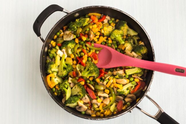 Colourful vegetables being cooked in a large frying pan.