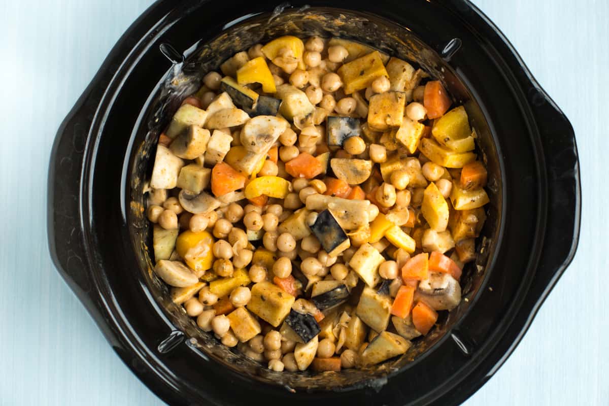Uncooked vegetables and chickpeas in a slow cooker pot.