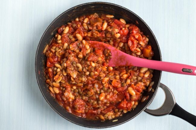 Lentils and beans cooking in a frying pan with tinned tomatoes.