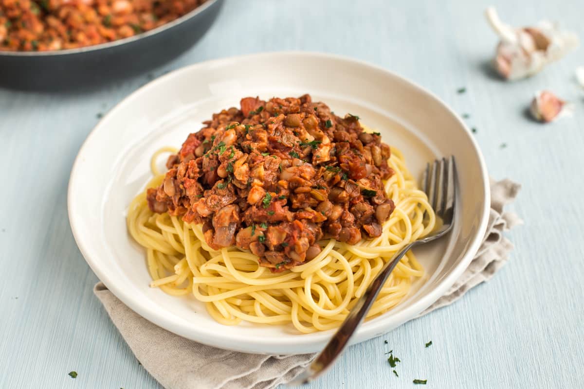Portion of walnut and bean bolognese neatly spooned on top of spaghetti in a bowl.