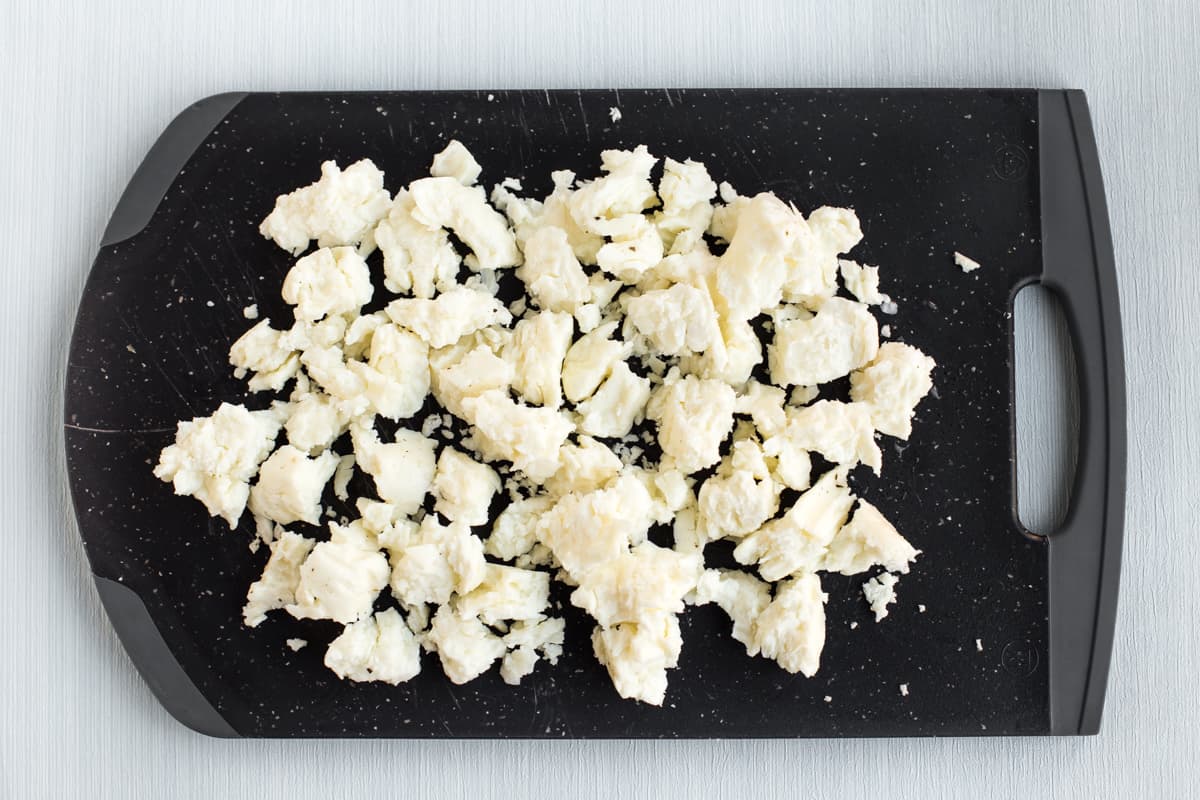 Crumbled halloumi cheese on a black chopping board.