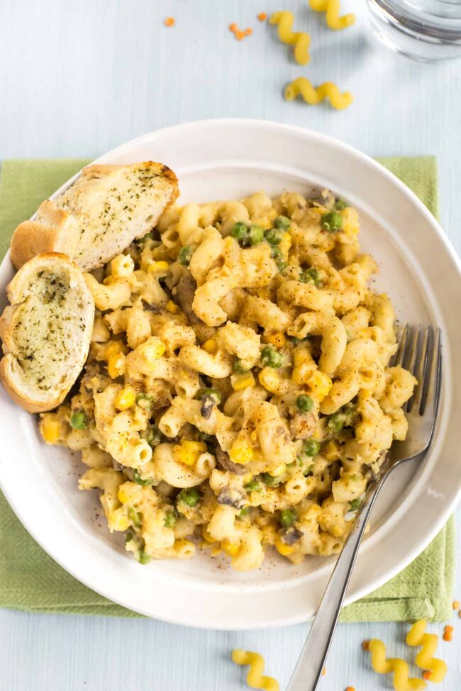 Portion of cheesy lentil pasta in a bowl with garlic bread.