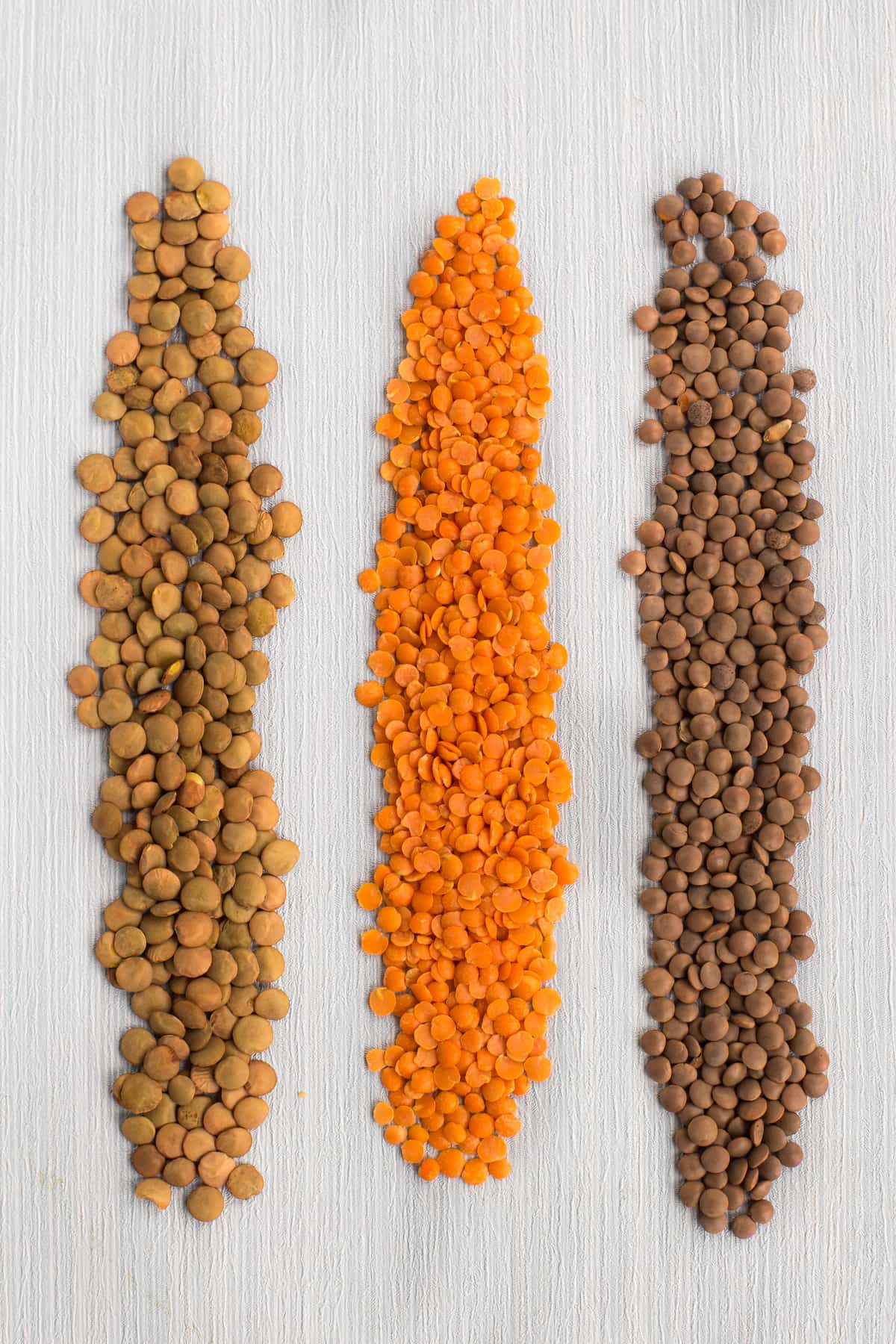 Green, red and brown lentils spread out on a surface to compare the differences.
