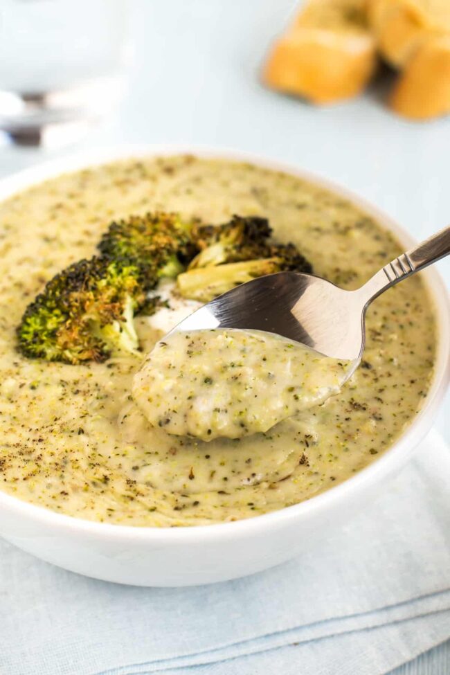 A spoon taking a scoop from a bowl of broccoli cheddar soup.