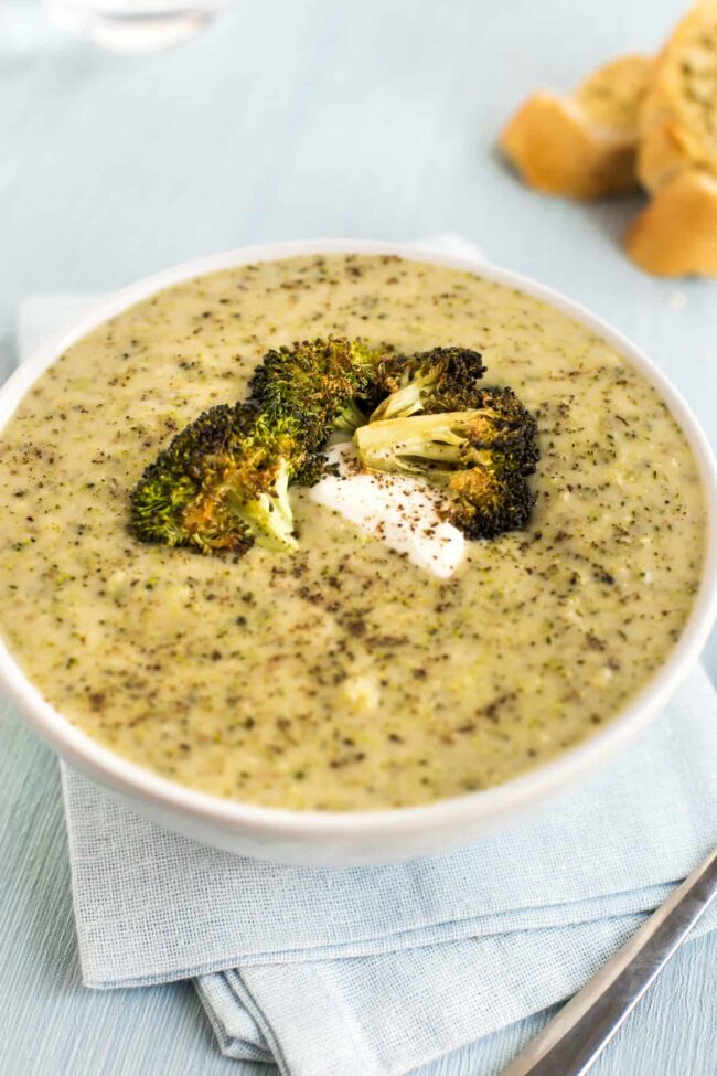 Cheesy broccoli soup in a bowl with roasted broccoli and sour cream.