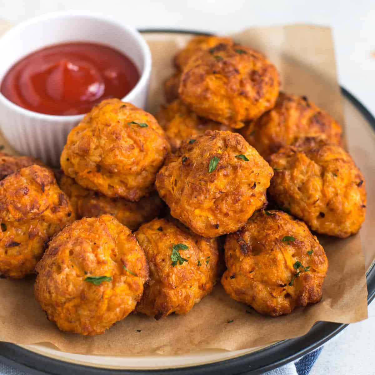 A stack of cheesy carrot bites on a plate with a ramekin of ketchup.