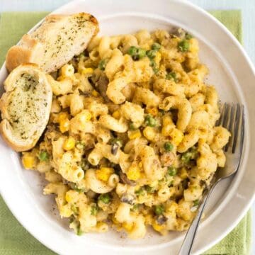 A portion of cheesy lentil pasta with peas in a bowl, served with garlic bread.