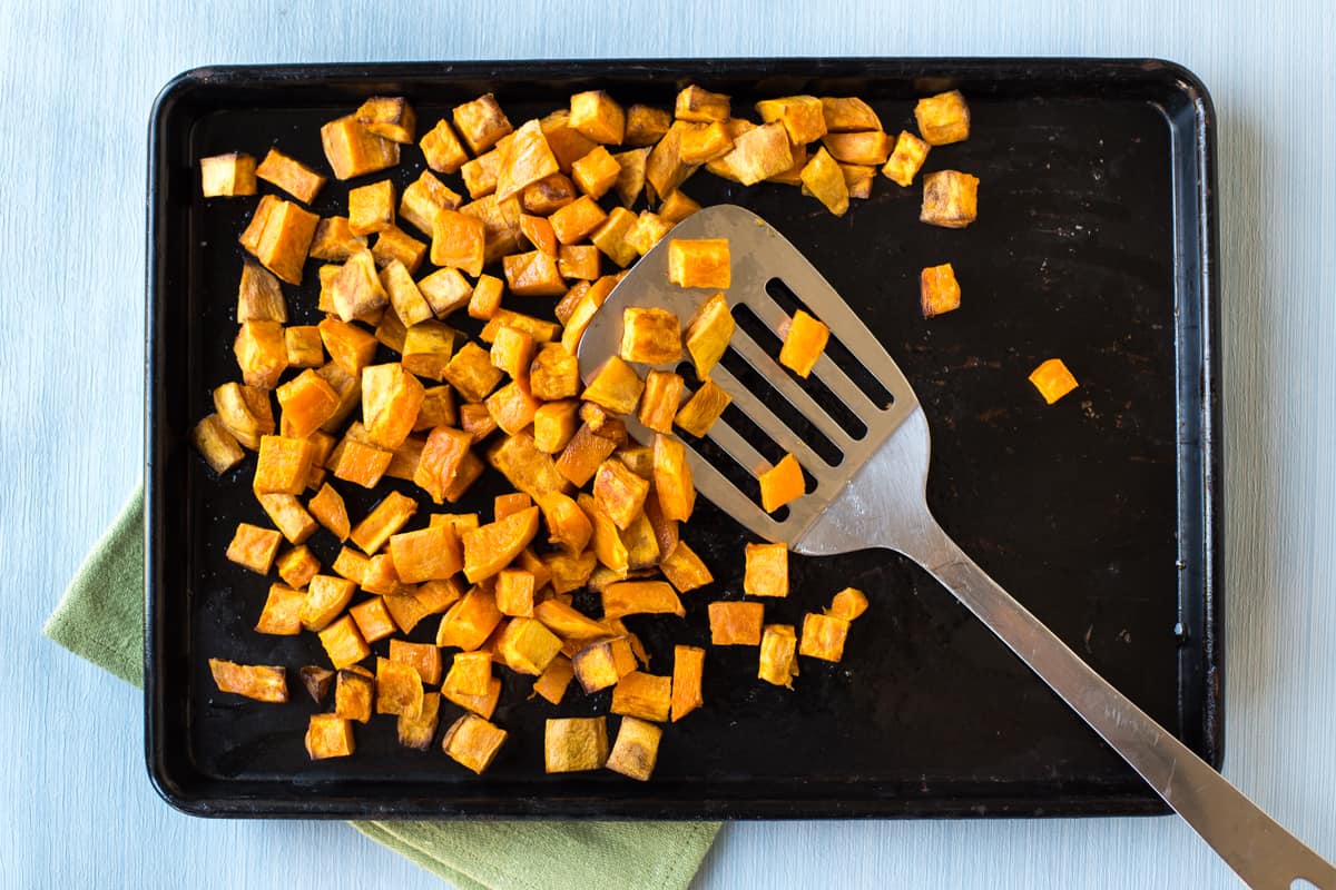 Diced sweet potato roasted on a baking tray with a metal spatula.