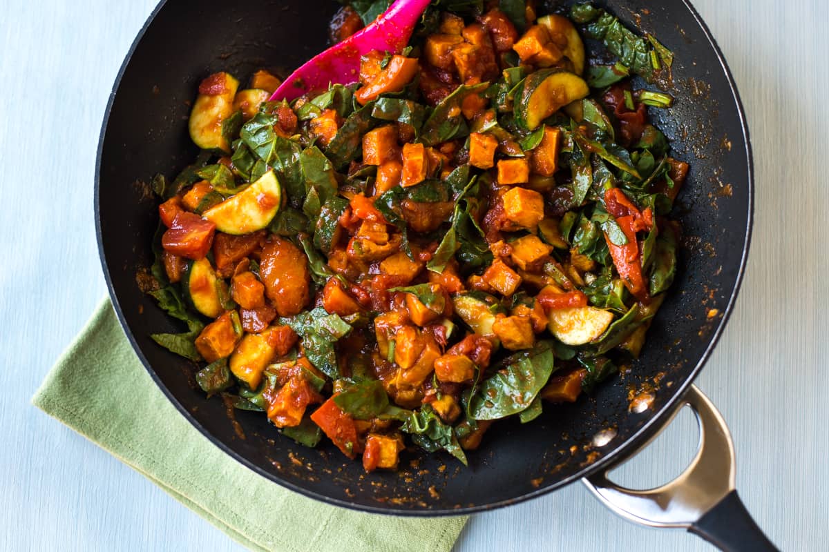 Sweet potato and spinach curry in a wok before being simmered.