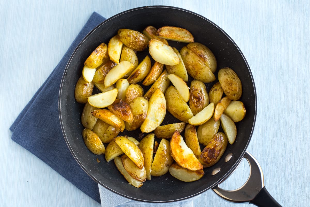 Crispy fried potato wedges in a frying pan.