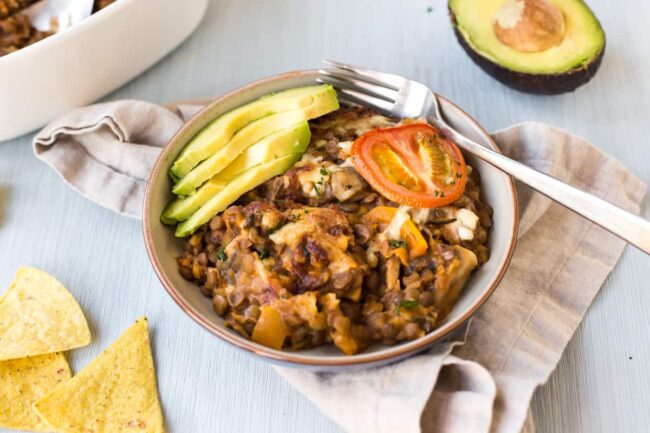 Portion of enchilada lentil casserole in a bowl topped with fresh avocado.