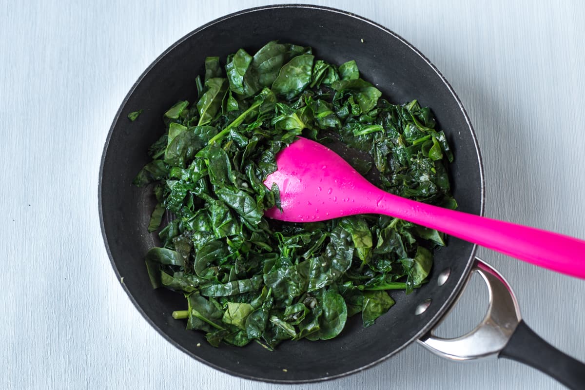 Spinach cooking in a frying pan with garlic.