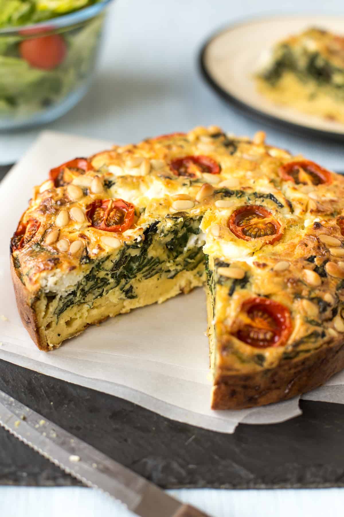 A spinach and tomato quiche with a slice removed.